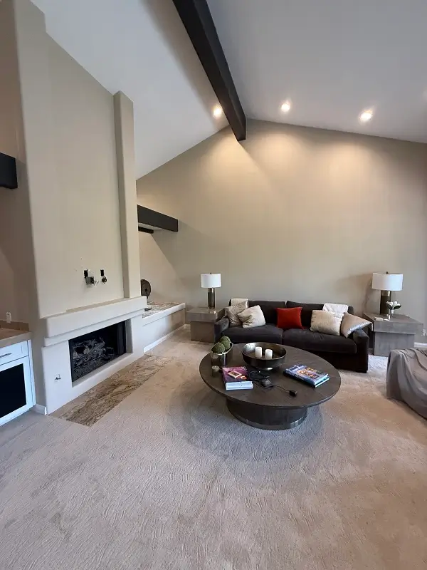 Well lit living room with carpet and high ceiling. Fireplace.
